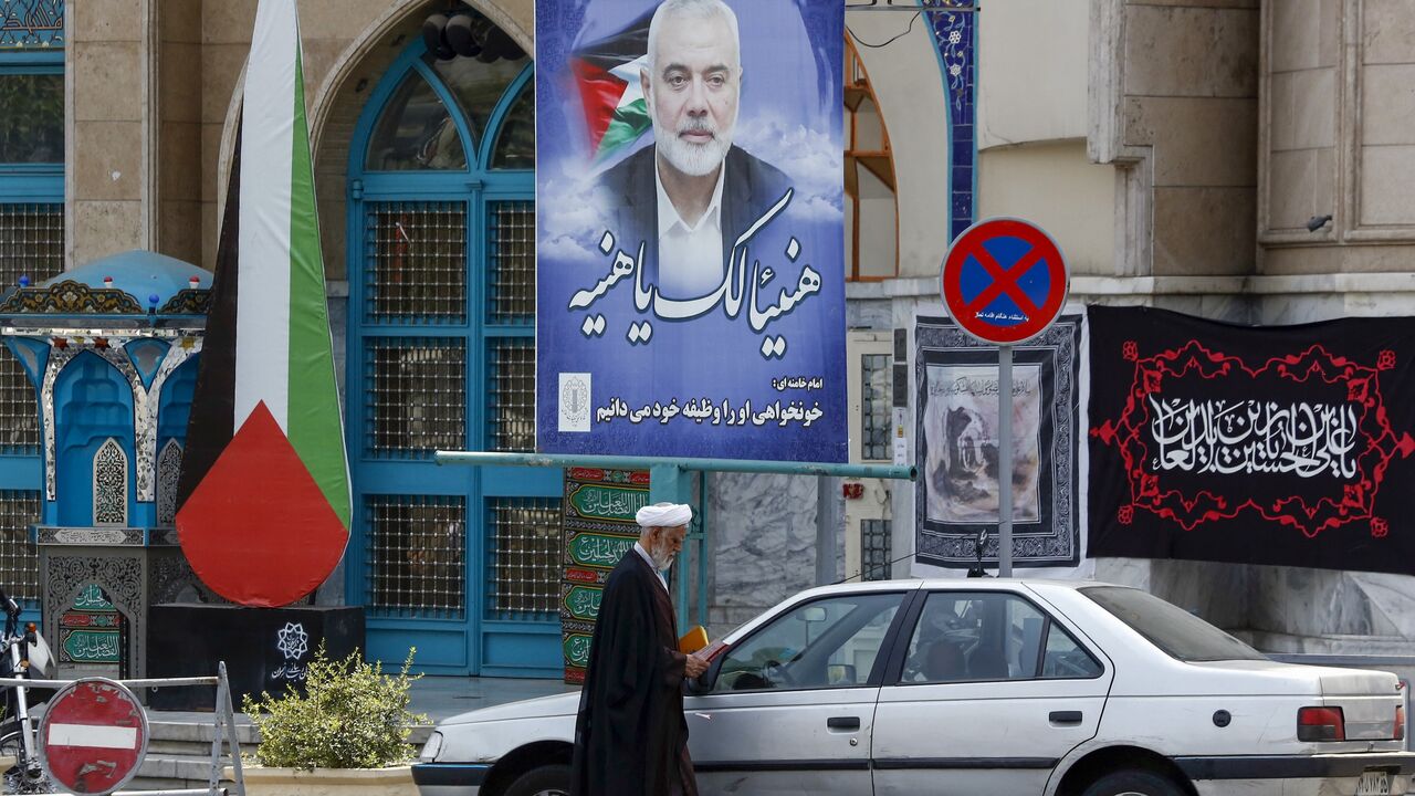 A cleric stands next to a poster depicting slain leader of the Palestinian Hamas group Ismail Haniyeh at Tehran's Palestine square on August 8, 2024. 